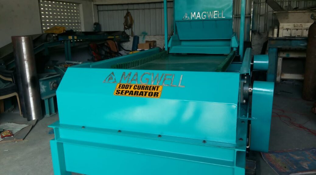 Industrial eddy current separator machine sorting non-ferrous metals on a conveyor belt.