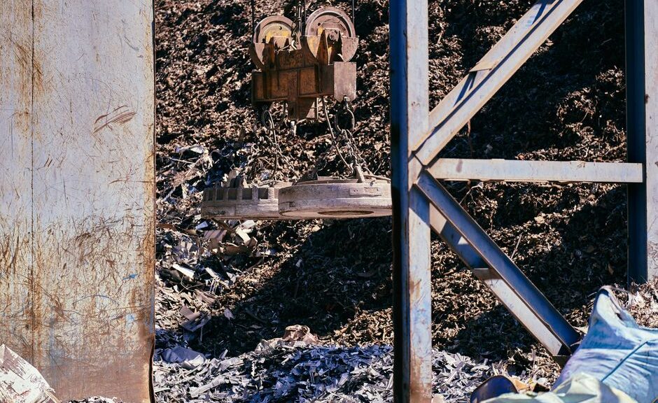 Magnetic crane sorting metal in an industrial scrapyard. Bright daylight highlights the steel and machinery.