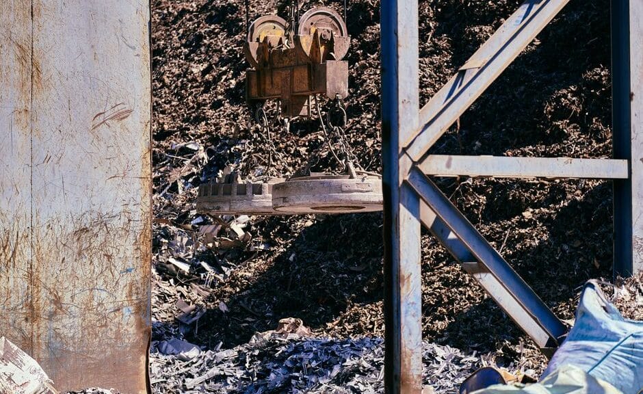 Magnetic crane sorting metal in an industrial scrapyard. Bright daylight highlights the steel and machinery.